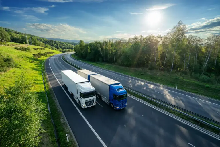 Zwei LKWs fahren auf einer Autobahn durch eine grüne Landschaft bei Sonnenlicht.
